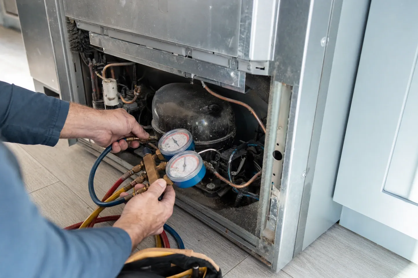 Manifold gauges connected to the compressor of a built-in refrigerator with the lower panel removed