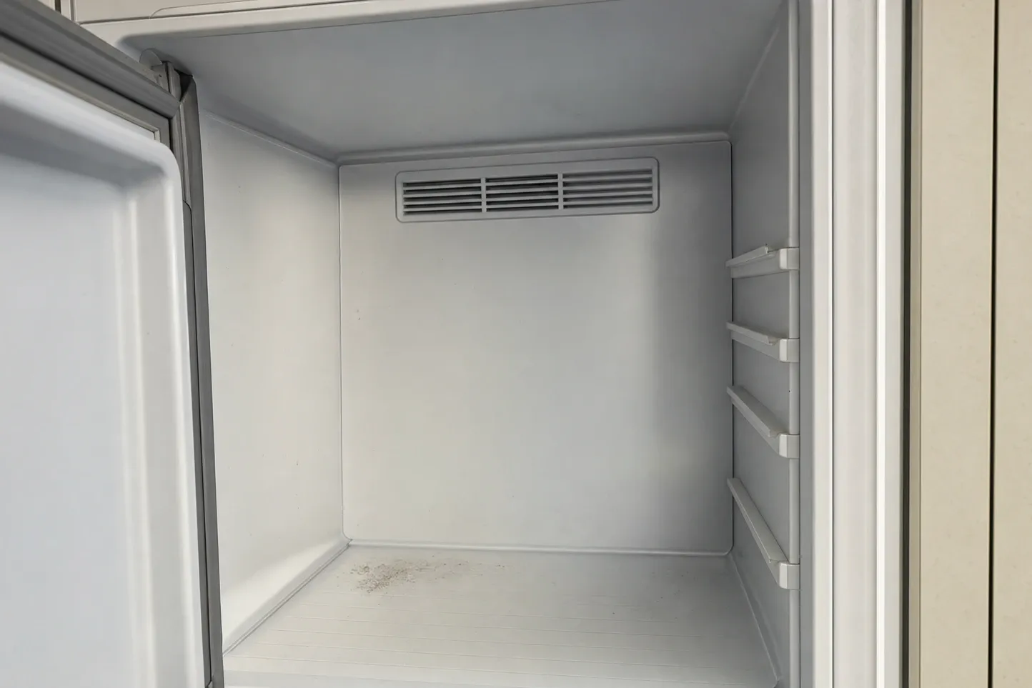 Empty refrigerated compartment interior with a rear air-vent grille and moulded door shelf rails